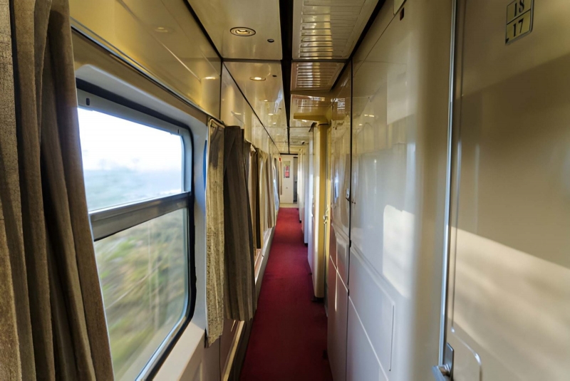 Corridor of a sleeper train carriage with a red carpet and a window